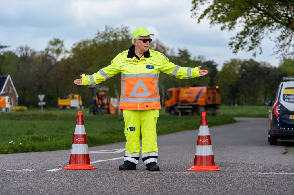 Verkeersregelaar in fluorescerende werkkleding regelt het verkeer tussen twee verkeerskegels tijdens wegwerkzaamheden.