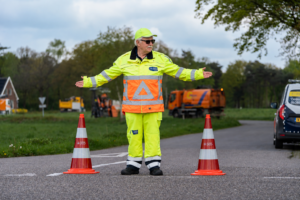Verkeersregelaar in fluorescerende werkkleding regelt het verkeer tussen twee verkeerskegels tijdens wegwerkzaamheden.