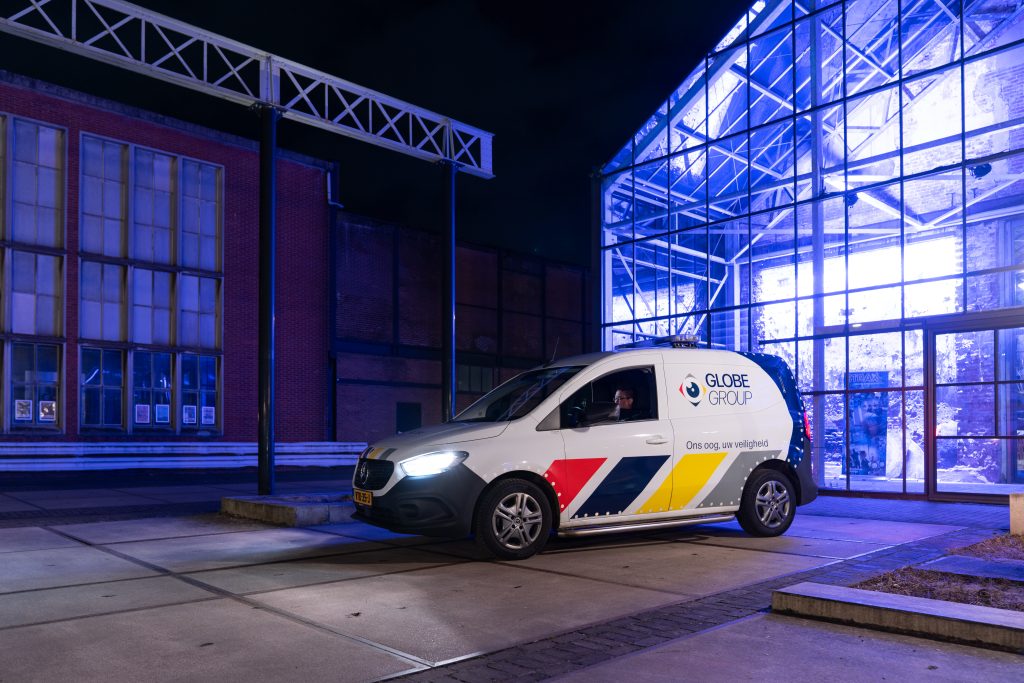 Surveillanceauto van Globe Group bij nacht voor een verlicht gebouw.
