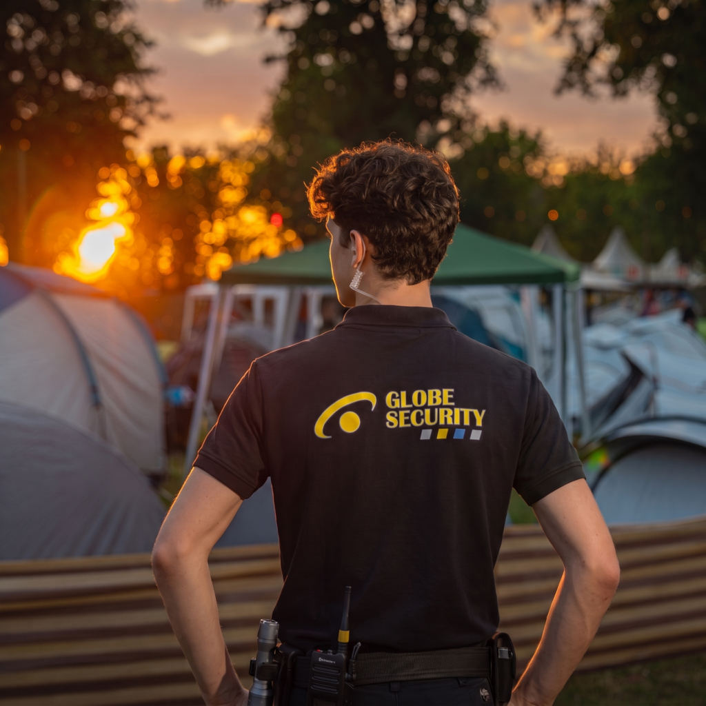 Beveiliger van Globe Security houdt toezicht op een evenemententerrein met tenten tijdens zonsondergang.