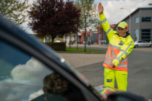 Verkeersregelaar in fluorescerende kleding geeft aanwijzingen aan automobilist op straat