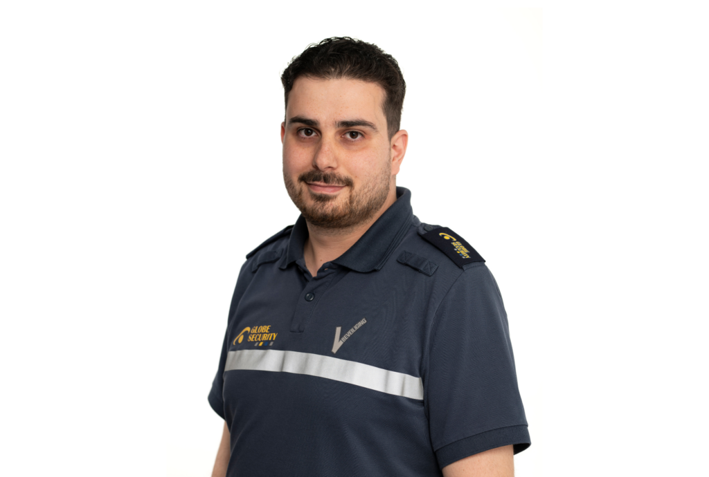 Professionele beveiliger in donkerblauw Globe Security-uniform, gefotografeerd tegen een lichte neutrale achtergrond.