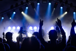 Publiek bij een liveconcert met opgestoken handen en fel verlichte podiumverlichting.