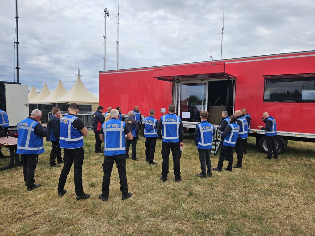 Beveiligingsmedewerkers van Globe Security tijdens een briefing bij een rode mobiele unit op een evenemententerrein.